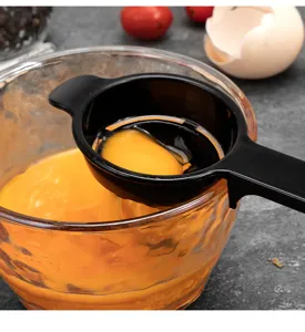 Detail view of a black plastic kitchen egg white separator tool resting on a clear glass bowl.