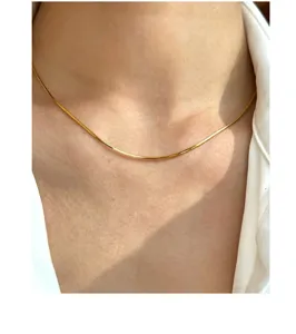 Detaillierte Nahaufnahme einer filigranen goldenen Schlangenkette am Hals getragen.