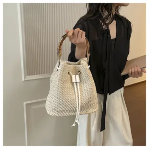 Gros plan détaillé d'un sac seau en paille élégant avec poignée bambou et cordon blanc.