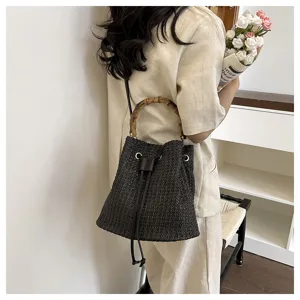 Gros-plan d'un sac seau en paille noire avec poignée en bambou unique et détail de cordon serré.