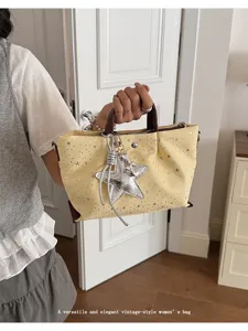 Detail view of the yellow canvas tote bag with star prints, silver star pendant and brown handles.