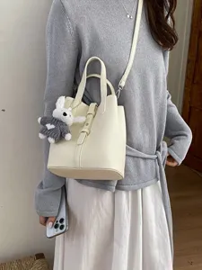 Minimalist cream leather bucket bag with handle and cute plush rabbit keychain for women.