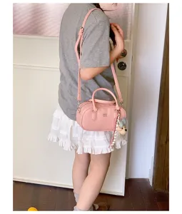 Pink leather bowling shoulder bag for women, stylish commuting crossbody handbag with charms.
