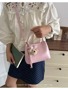 Trendy pink shoulder crossbody bucket bag for women with cute bear pendant and top handle.
