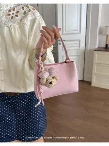 Close-up detail of a chic pink women's handbag featuring a cute teddy bear plush pendant.