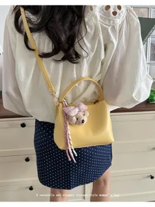 Detail view of stylish yellow bucket bag with cute bear charm and shoulder strap.