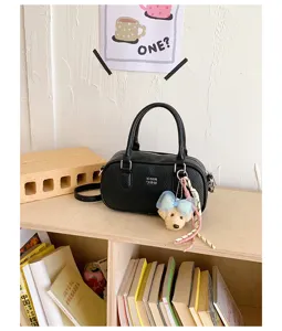 Detailed view of women's black leather bowling shoulder bag with cute bow charm on wooden shelf.