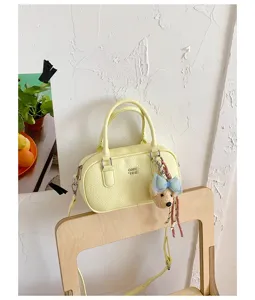 Fashionable light yellow leather bowling bag with cute bear charm, versatile crossbody handbag.