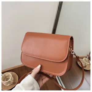 Detail shot of stylish brown leather crossbody shoulder bag with metal hardware and flap design.