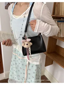 Detailed view of black PU leather shoulder bucket bag featuring cute plush bear pendant.