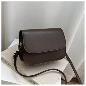 Detail shot of minimalist women's dark brown crossbody bag with elegant flap and strap.