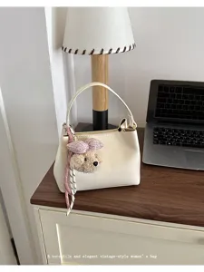 Detailed view of stylish women handbag with cute teddy charm, elegant cream bucket bag.