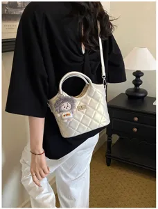 Élégant sac à bandoulière matelassé blanc avec fermoir en métal et pendentif poupée.