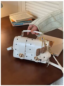 Detail view of white polka dot leather handbag with cute bear pendant and metal lock.