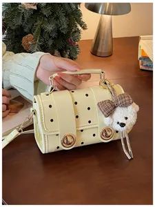 Close-up detail shot of the chic polka dot handbag featuring a cute plush bear pendant.