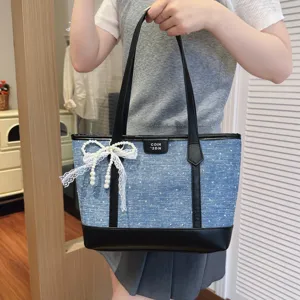 Casual denim tote bag for women with lace pearl bow and black leather handles detail.