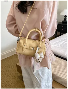 Vista dettagliata di una elegante borsa Boston gialla chiara con un grazioso ciondolo orsetto.
