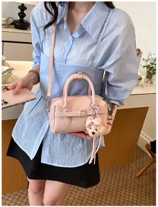 Delizioso dettaglio di borsa Boston rosa, con grazioso ciondolo in peluche e cintura elegante.
