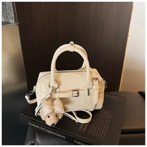 Dettaglio borsa Boston in pelle beige con ciondolo cagnolino di peluche e manici.