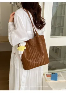 Detailed view of brown woven leather tote bag with stylish bear pendant in minimalist interior.