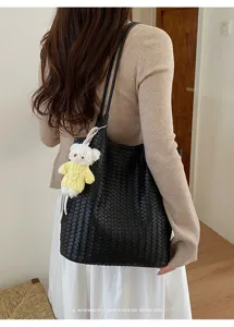 Detailed view of black woven leather tote bag with plush bear charm, minimalist retro style.