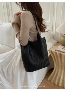 Detailed shot of elegant black woven leather tote bag in minimalist interior scene.