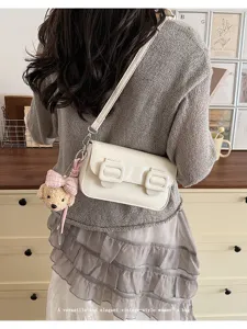 Detailed shot of a stylish white crossbody bag with double buckles and cute teddy bear charm.