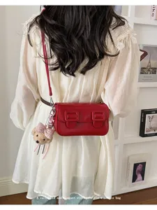 Detailed view of trendy red vintage crossbody bag with cute bear pendant and double buckle.