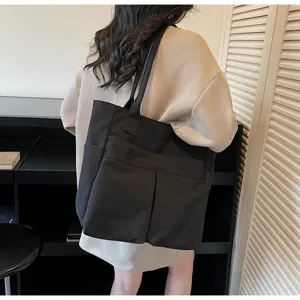 Primo piano dettagliato di una borsa tote nera casual con tasche anteriori e comodi spallacci.