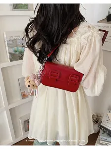 Detailed view of red vintage shoulder bag with double buckles and teddy bear charm.