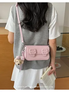 Detail view of a pink crossbody bag featuring dual buckle closure and cute bear charm.