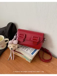 Red patent leather shoulder bag detail with cute bear charm and vintage double buckles.
