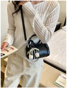 Minimalist black pillow shoulder bag with pearl tulip pendant detail, stylish daily accessory.