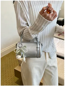 Stylish silver cylindrical pillow bag with pearl ribbon pendant, chic shoulder crossbody bag.
