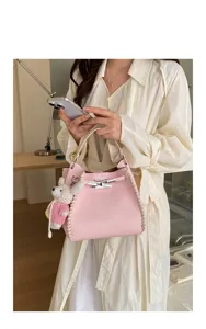 Pink leather bucket handbag with white edge stitching and cute rabbit charm for women commute daily use.