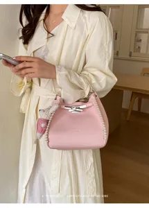Stylish pink leather bucket bag with woven details, metal lock, and cute bear pendant.