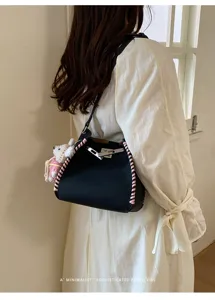 Detail shot of black leather shoulder bag with pink braided edges, metal lock and cute charm.
