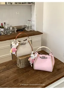 Stylish litchi pattern leather handbag with woven side details and cute plush rabbit charm.