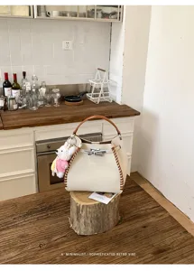Chic contrast color bucket bag with woven side details and plush bear charm for daily commute.