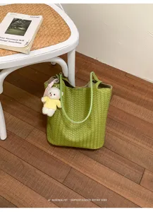 Green woven leather tote bag detail, minimalist shoulder bag with cute bear charm on wooden floor.