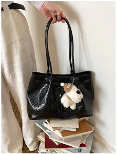 Detail view of black woven shoulder tote bag featuring a cute plush dog pendant accessory.