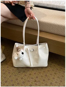 Detailed view of white woven tote bag featuring soft shoulder straps and cute puppy charm.