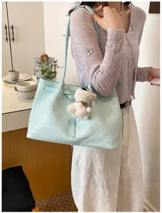 Detail view of light blue woven tote bag with cute bear pendant in a chic daily scene.