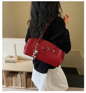 Red leather shoulder bag detail showing structured design, metal buckle and cute charm.