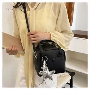 Detail shot of a black textured crossbody handbag featuring stylish silver star charms and handles.