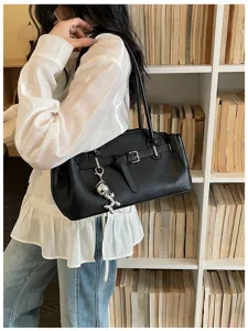 Stylish black leather shoulder bag detail featuring metal buckle and silver balloon dog charm.