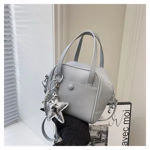 Detailed view of grey textured leather mini handbag with top handles and star charm.