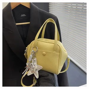 Yellow leather crossbody bag detail, featuring double top handles and a silver star charm.