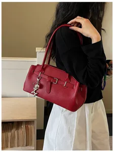 Detailed shot of red leather shoulder bag with chic metal buckle and playful charm.