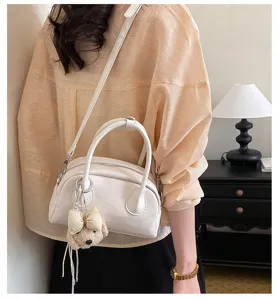 Detail shot of stylish white shoulder bag with cute plush bow bear charm in elegant room.